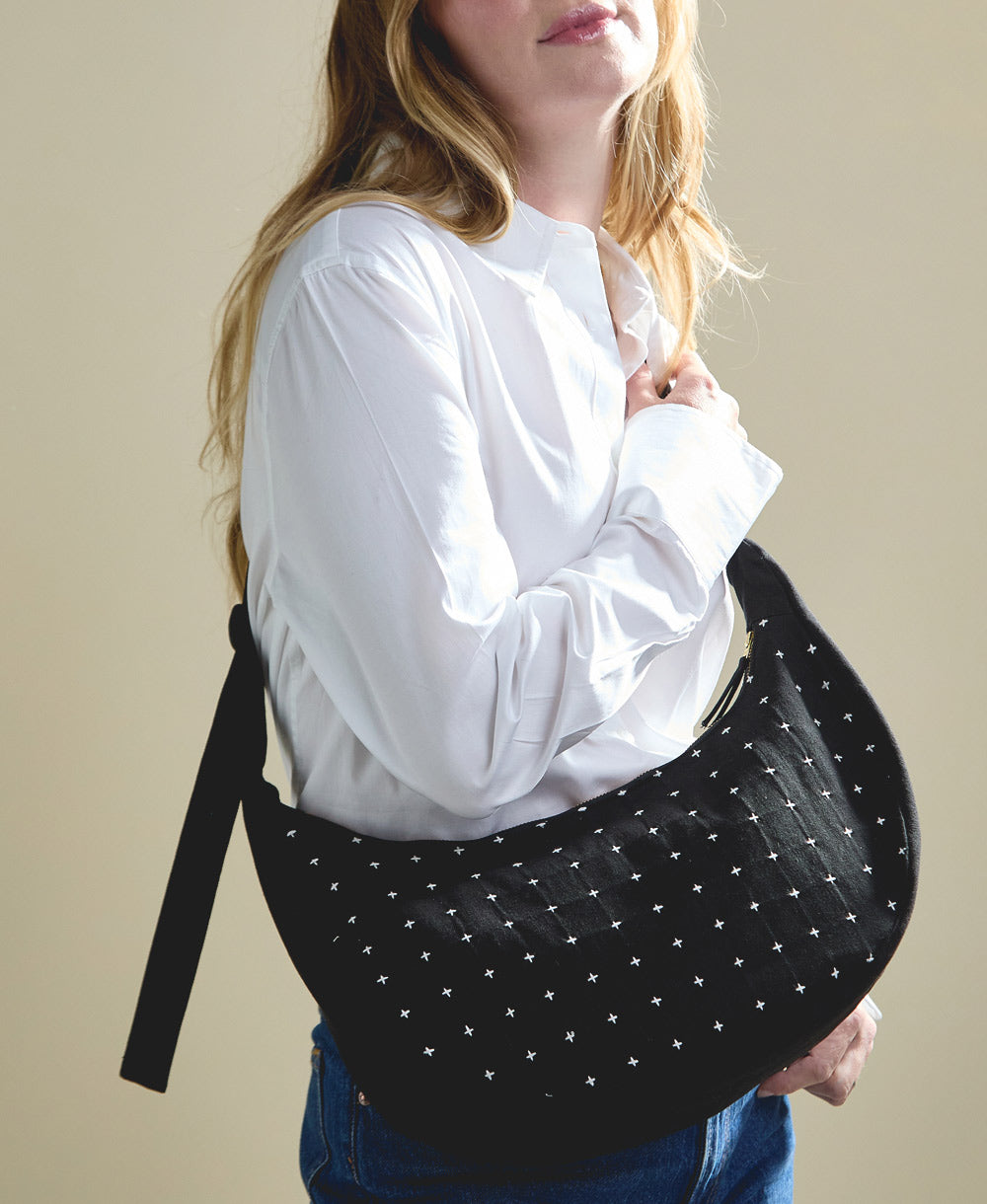 sustainable crescent bag in black with white embroidery slung over woman's shoulder