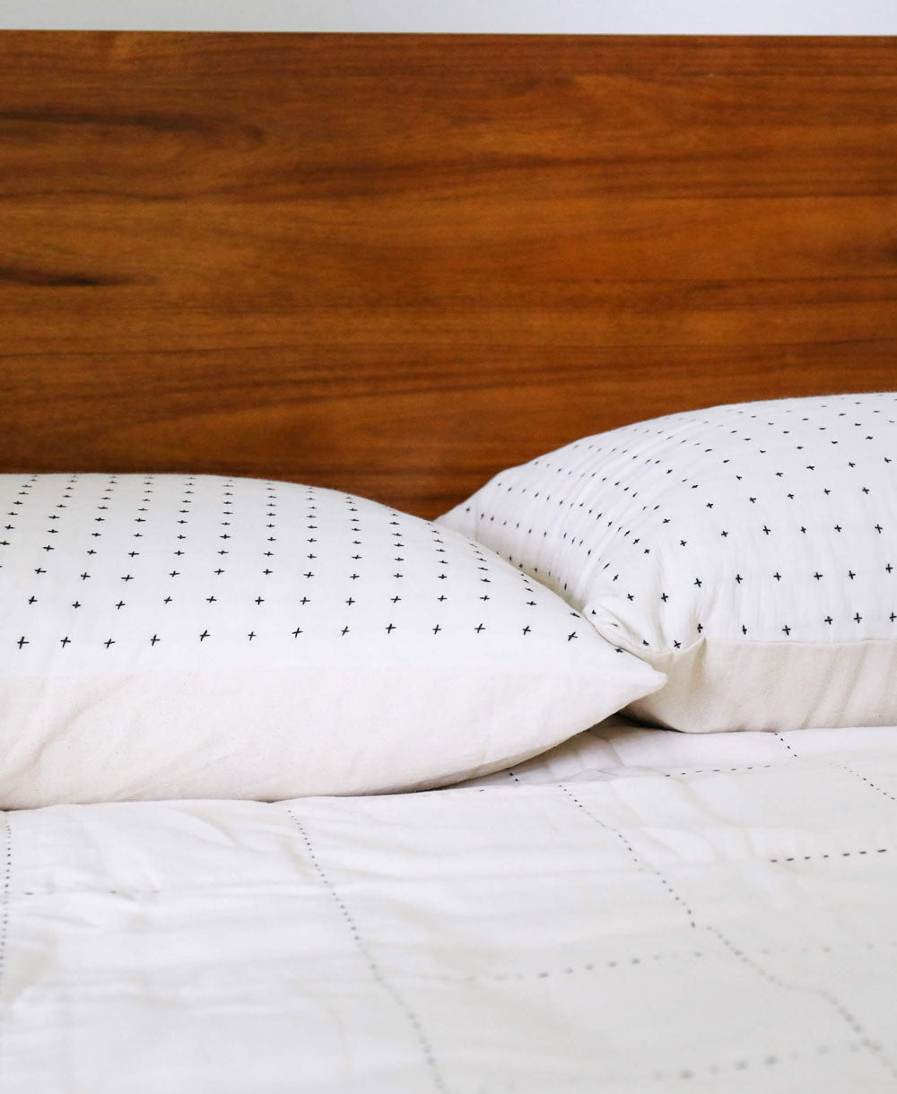 white quilt on bed with wooden headboard with matching cross-stitch standard pillow shams