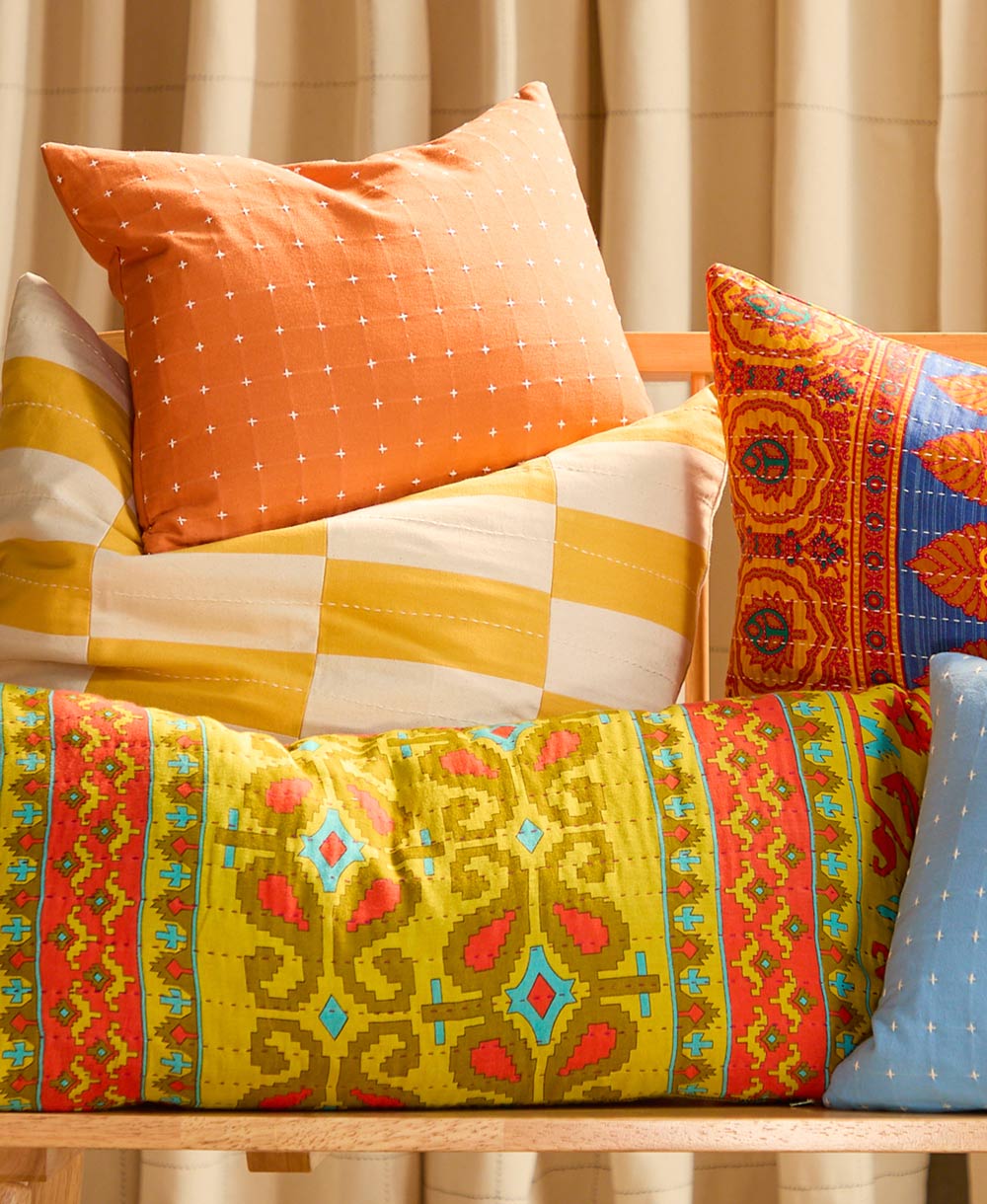 apricot cross stitch small pillow on top of other colorful bright pillows