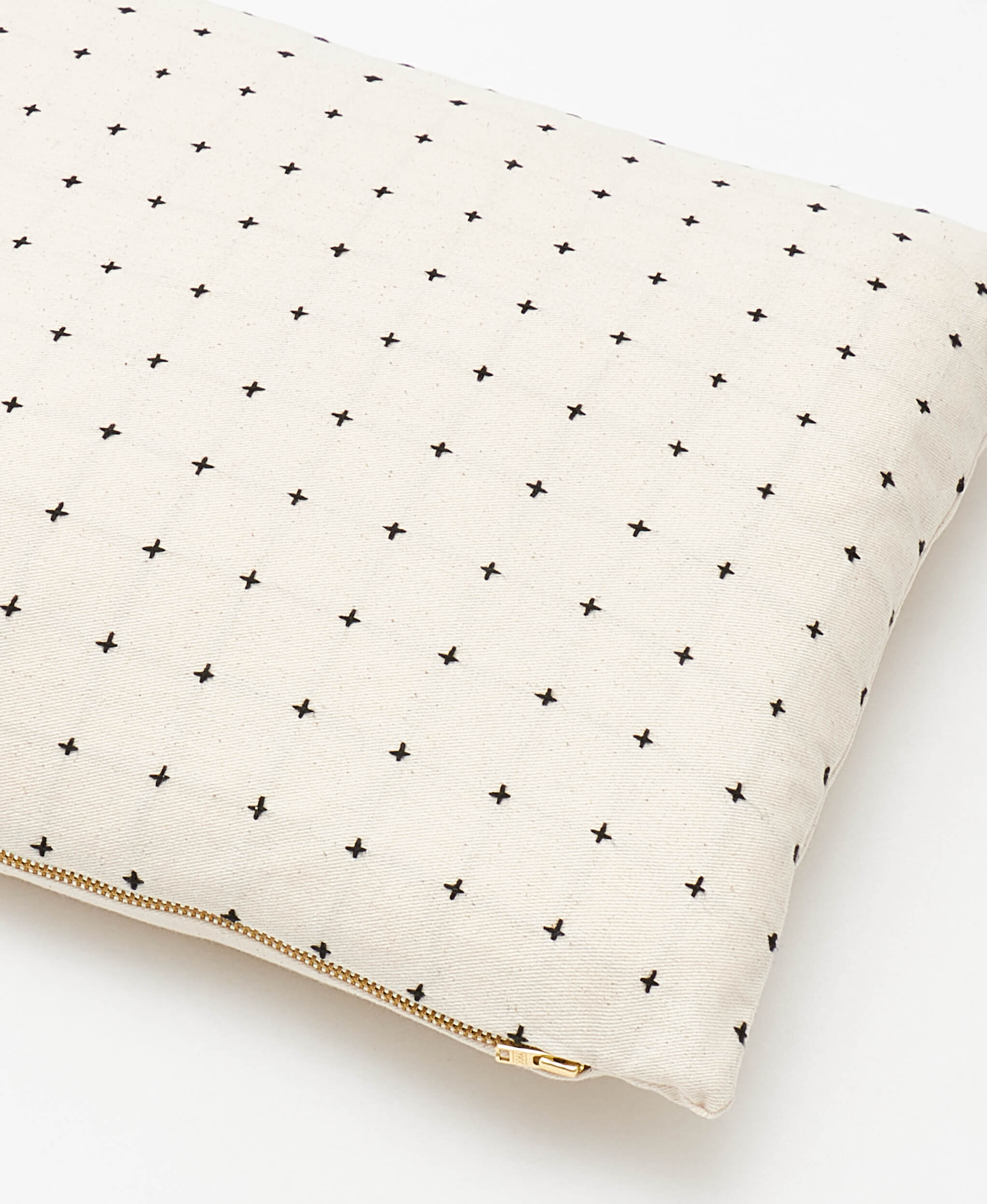 close up of ivory small pillow with black cross-stitch embroidery and brass toned metal zipper closure