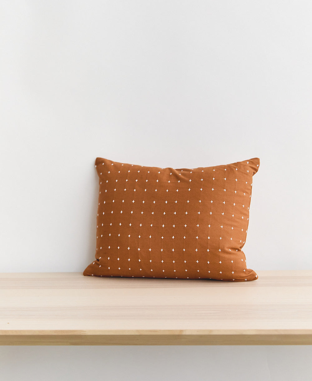 camel brown cross-stitch small pillow sitting on light wooden entryway bench