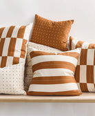 Set of brown and white patterned pillows on a wooden entry way bench against a light background