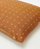 brown small pillow with white cross-stitch pattern and brass toned zipper closure