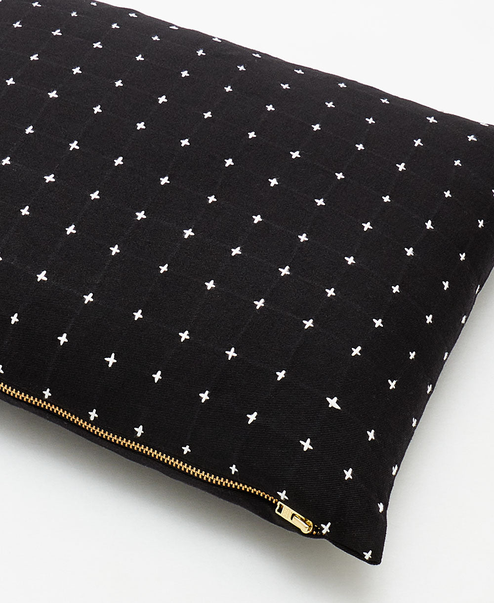 close up detail of black small pillow with white cross-stitch embroidery and brass toned zipper closure