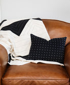 Black and white patterned pillow on a brown leather couch with a matching patchwork quilt