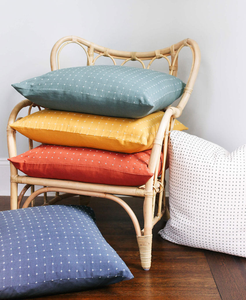 Rattan chair with colorful cushions on a wooden floor against a light gray wall
