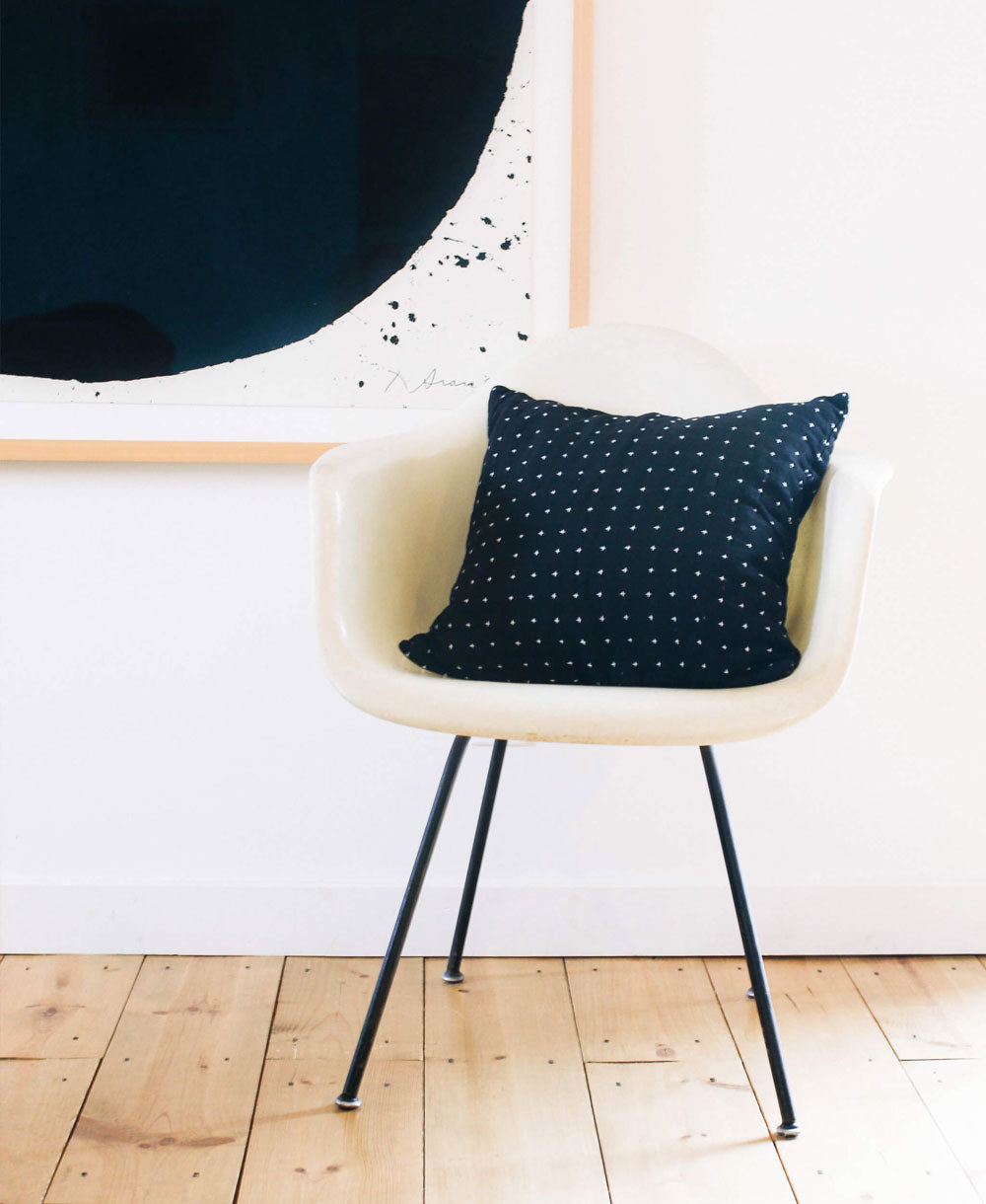 modern white chair with a black throw pillow with tiny white cross-stitches