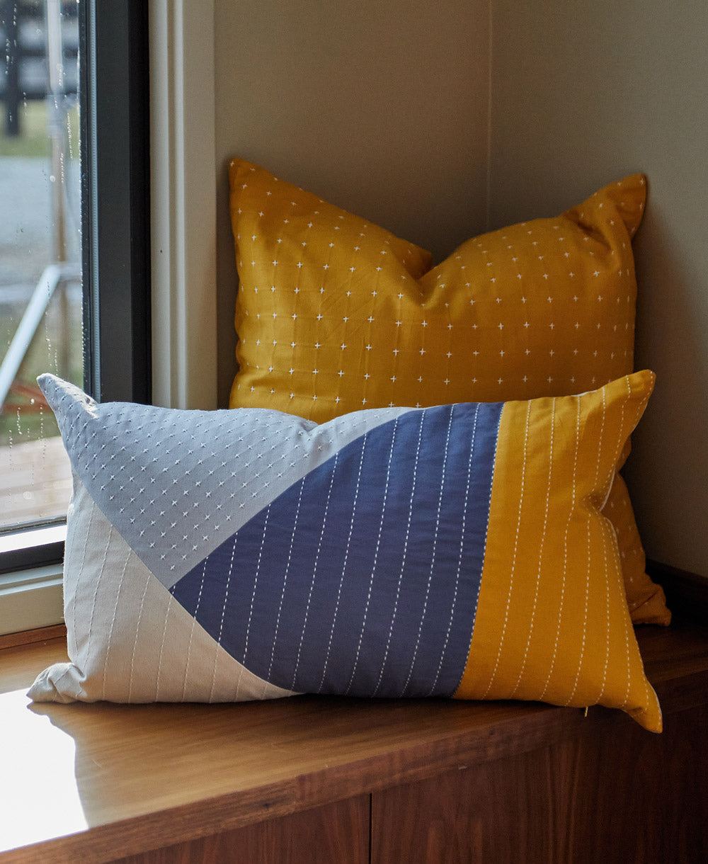 Two decorative pillows on a windowsill, one yellow with white dots and one multicolored