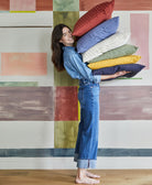 Woman holding a stack of colorful pillows against a geometric-patterned wall