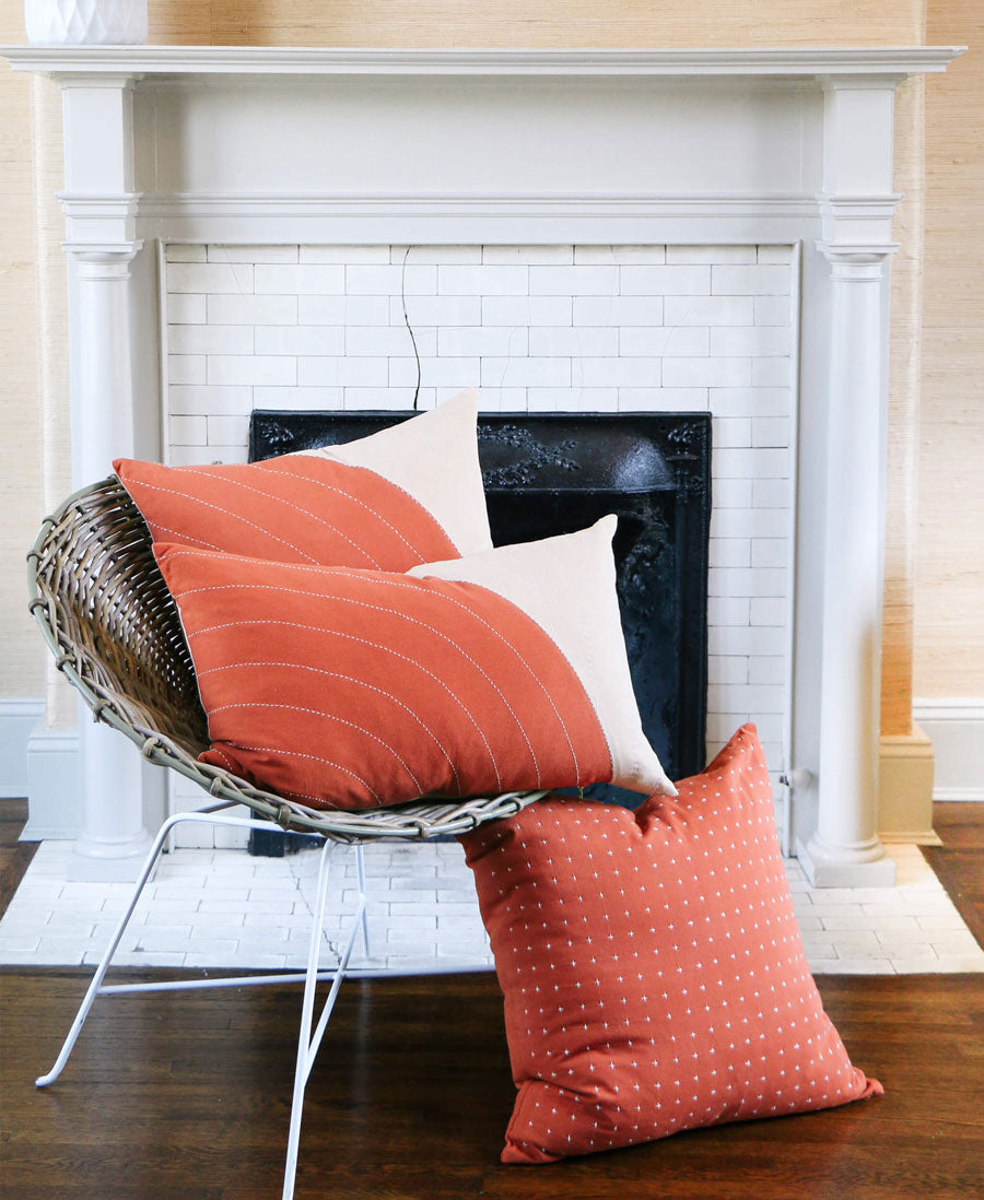 Wicker chair with orange cushions in front of a white fireplace