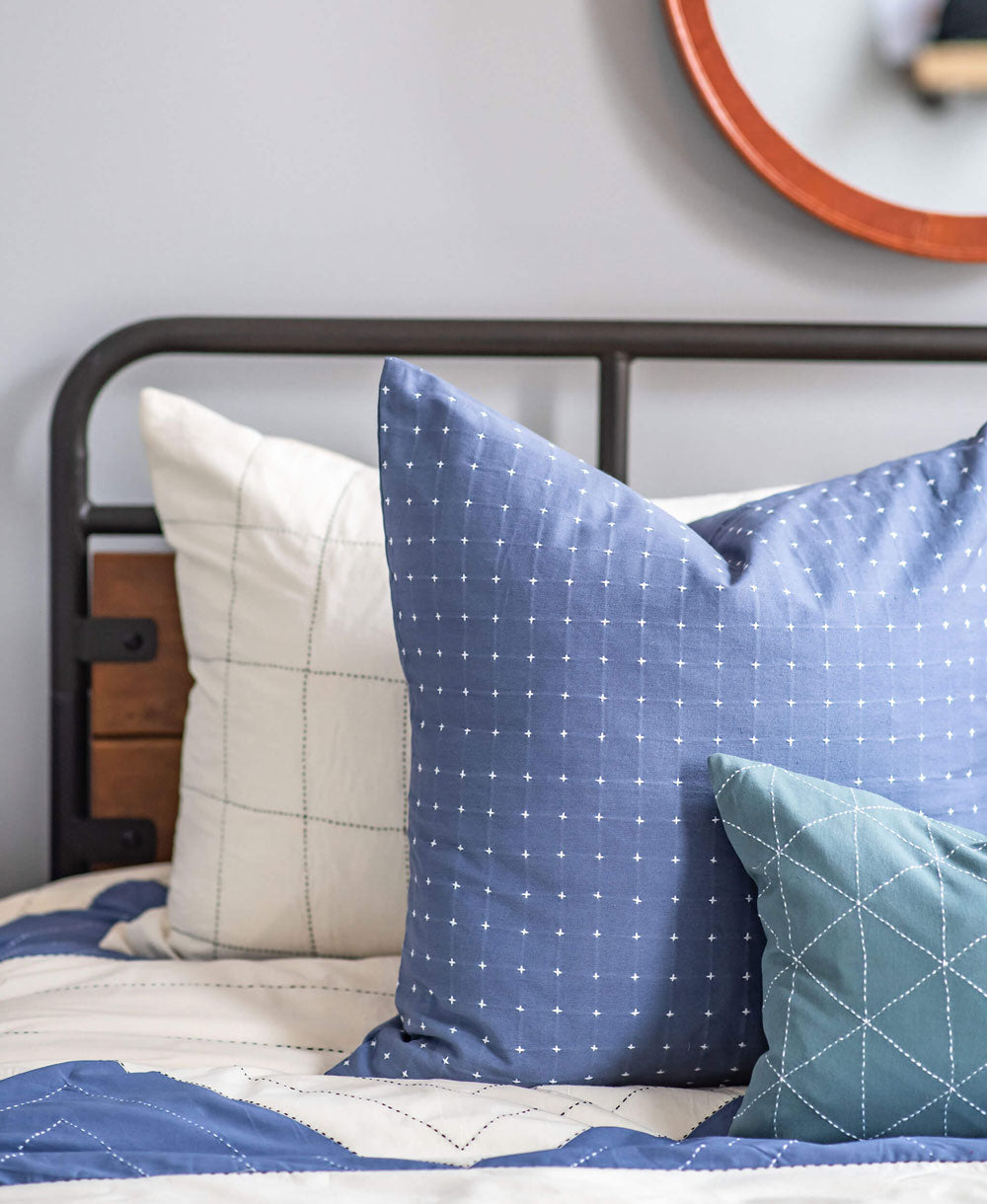Close-up of slate blue pillows on a bed with a neutral background