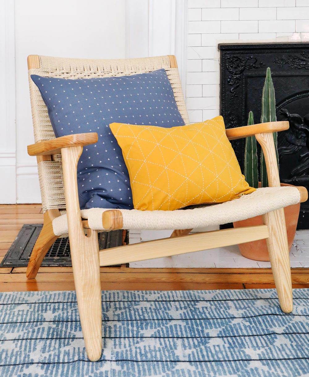 Wooden chair with blue and yellow cushions in a room with a fireplace and rug.
