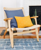 Wooden chair with blue and yellow cushions in a room with a fireplace and rug.