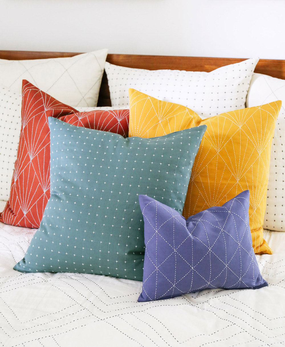 Colorful pillows on an all white bed with a wooden headboard