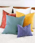 Colorful pillows on an all white bed with a wooden headboard