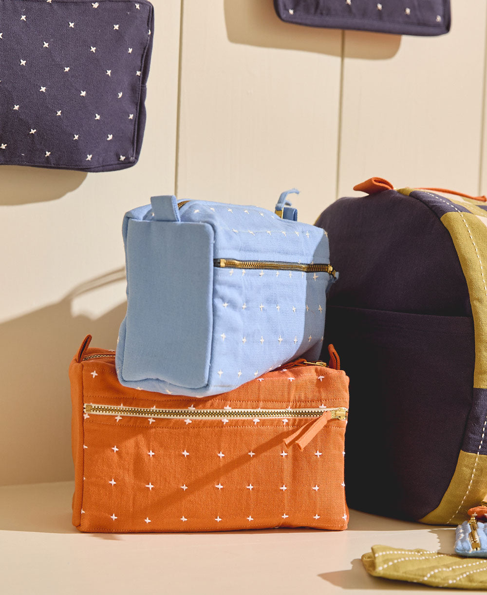 sky blue and orange toiletry bag stacked on top of one another with white cross-stitch pattern