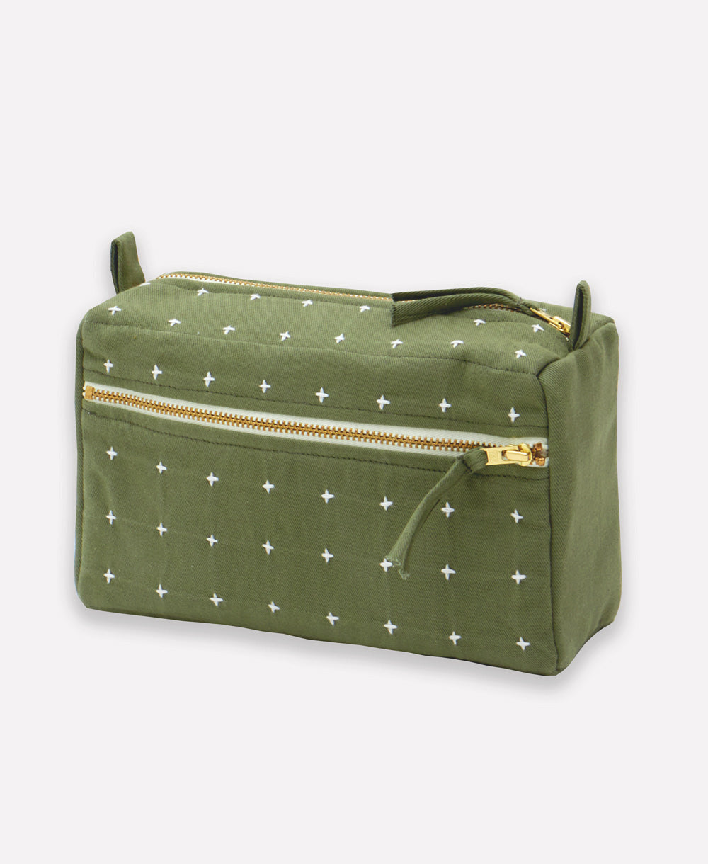 pine green toiletry bag with white cross-stitch pattern and gold zipper on a light gray background