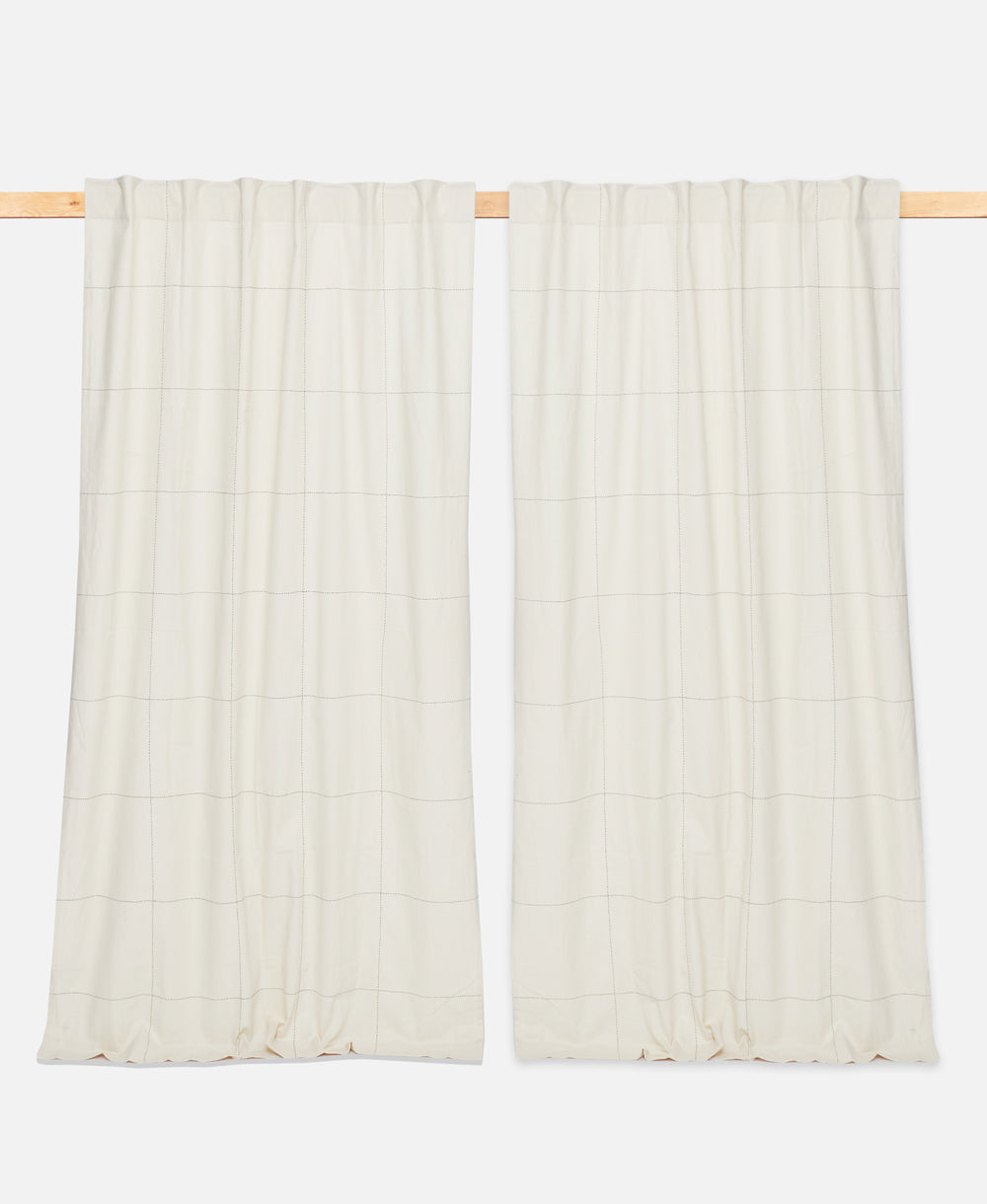 Two white textured curtains hanging on a wooden rod against a white background