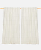 Two white textured curtains hanging on a wooden rod against a white background