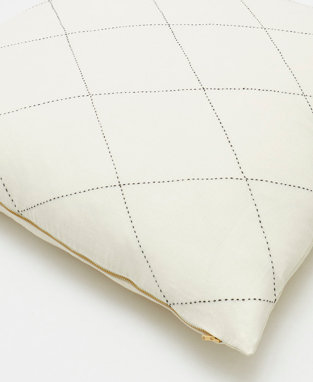 Quilted white pillow with gold trim on a light background