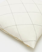 Quilted white pillow with gold trim on a light background