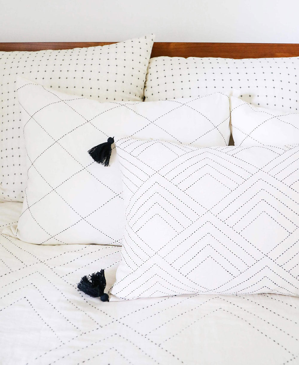 White quilted pillow with black tassels on a bed with white bedding.