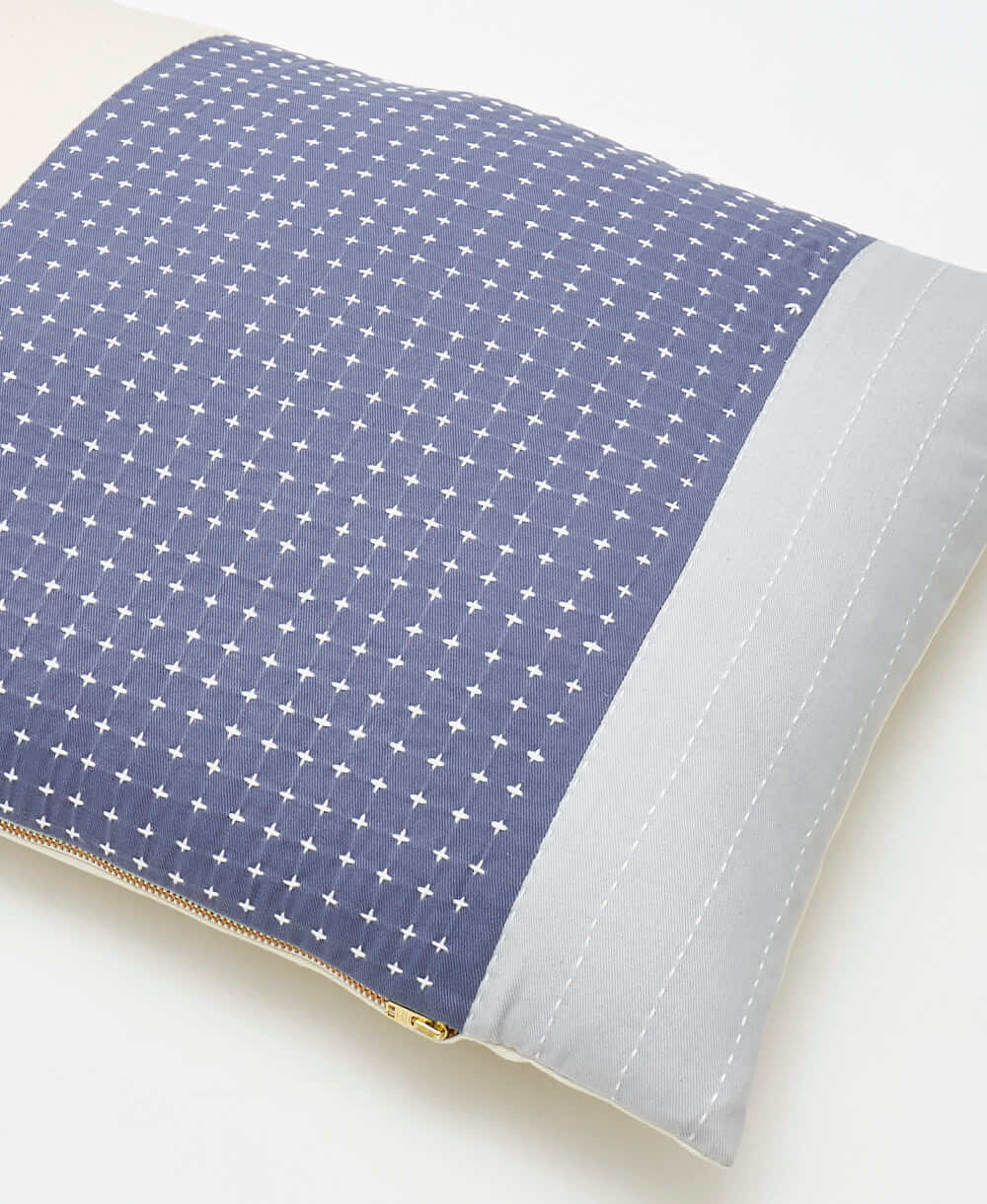 light blue and slate blue throw pillow with tiny white cross-stitch pattern and brass toned metal zipper