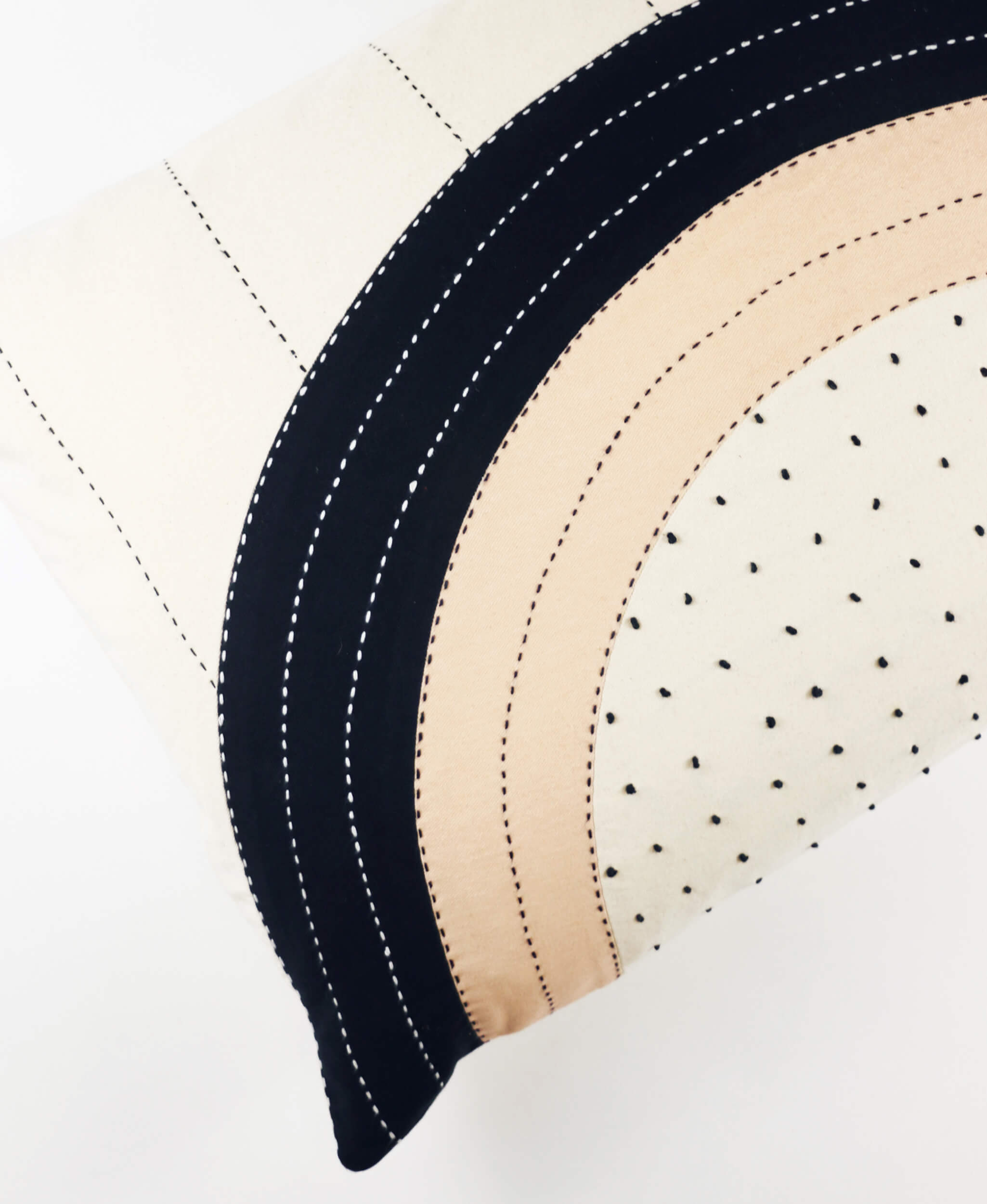 Close-up of a quilted fabric with black, beige, and white stitching on a white background