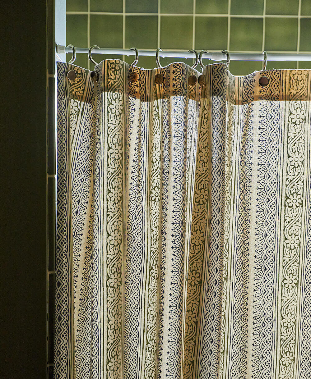 Decorative shower curtain with intricate patterns and gold accents against a tiled bathroom wall.