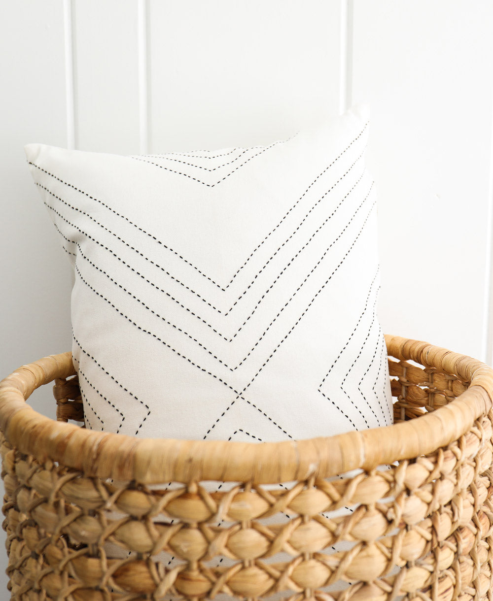 White pillow with black zigzag pattern in a woven basket against a white wall