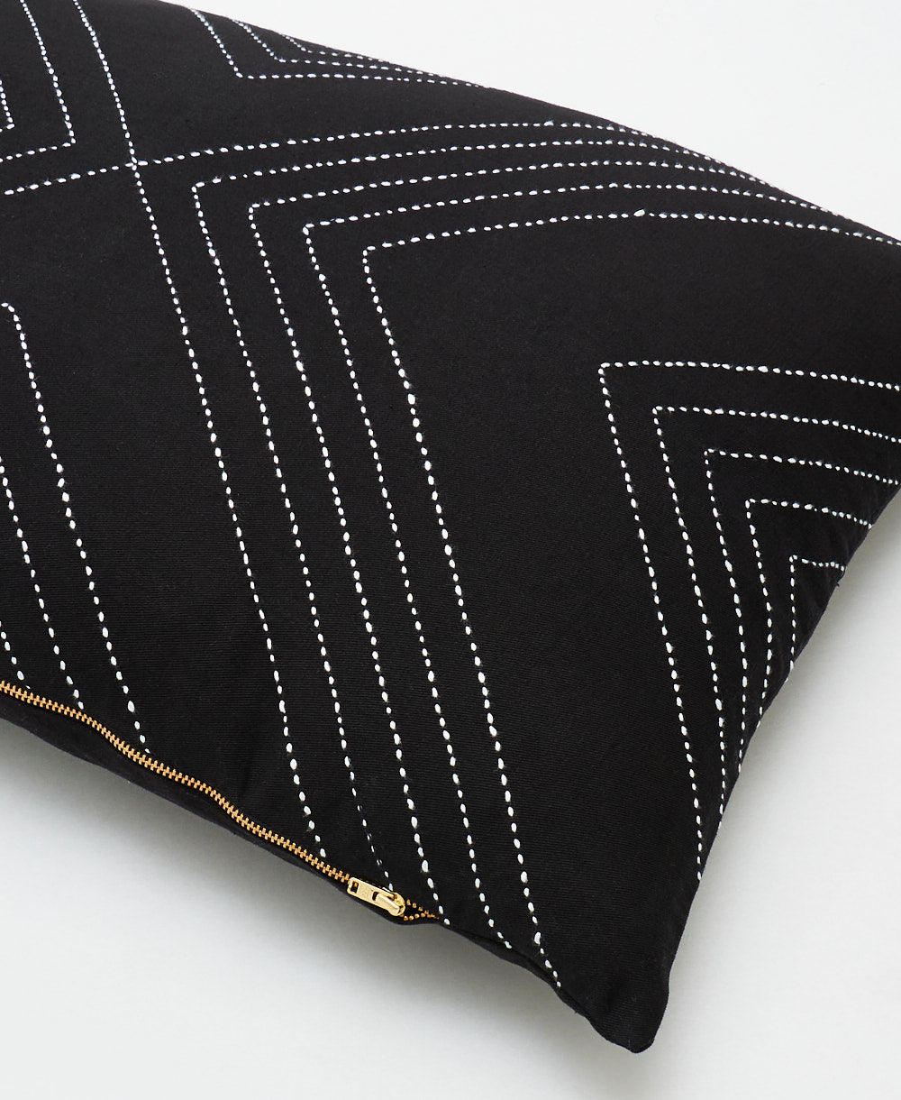 Black pillow with white geometric stitching on a light gray background