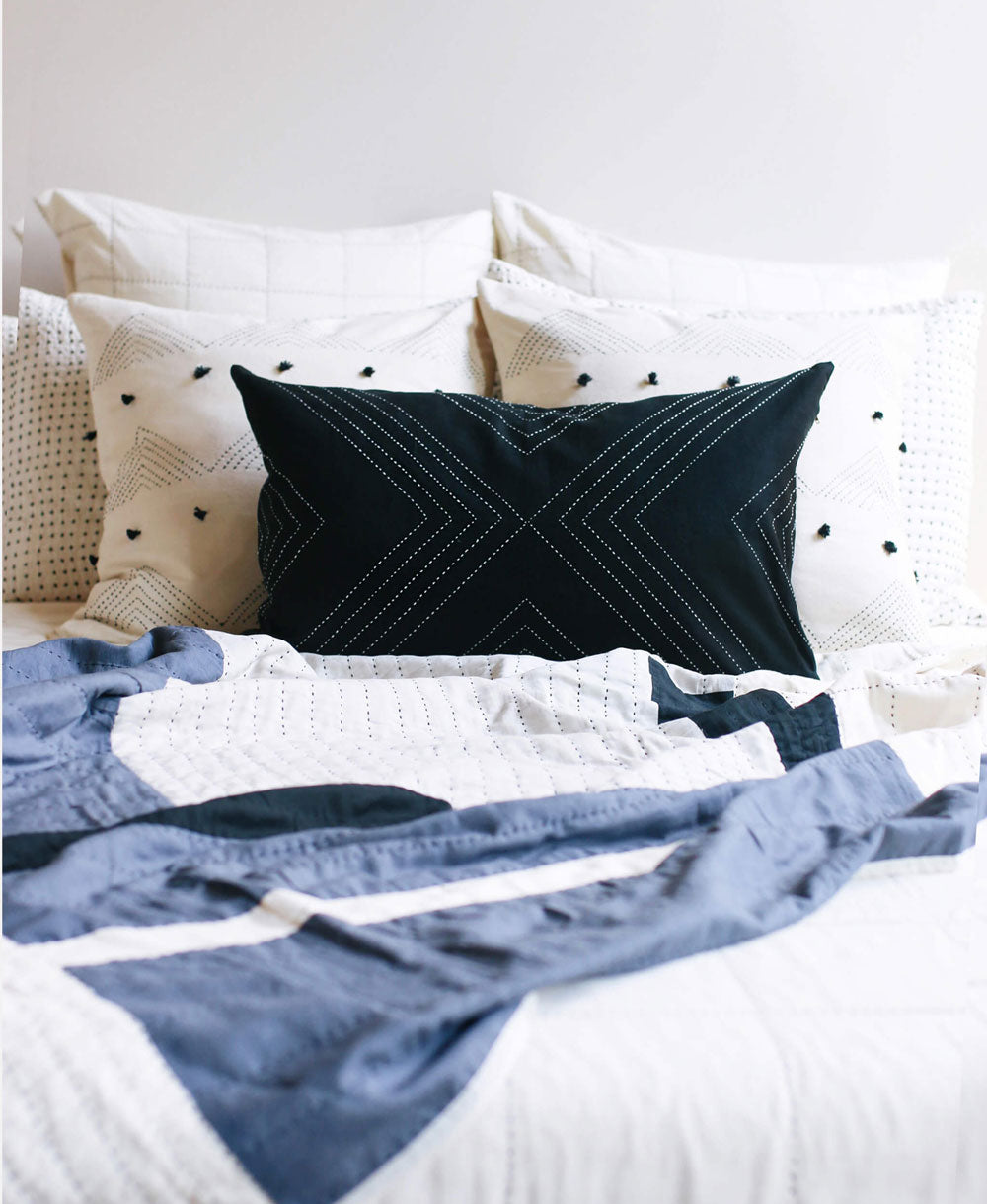 Black pillow with geometric pattern on a bed with white and blue bedding