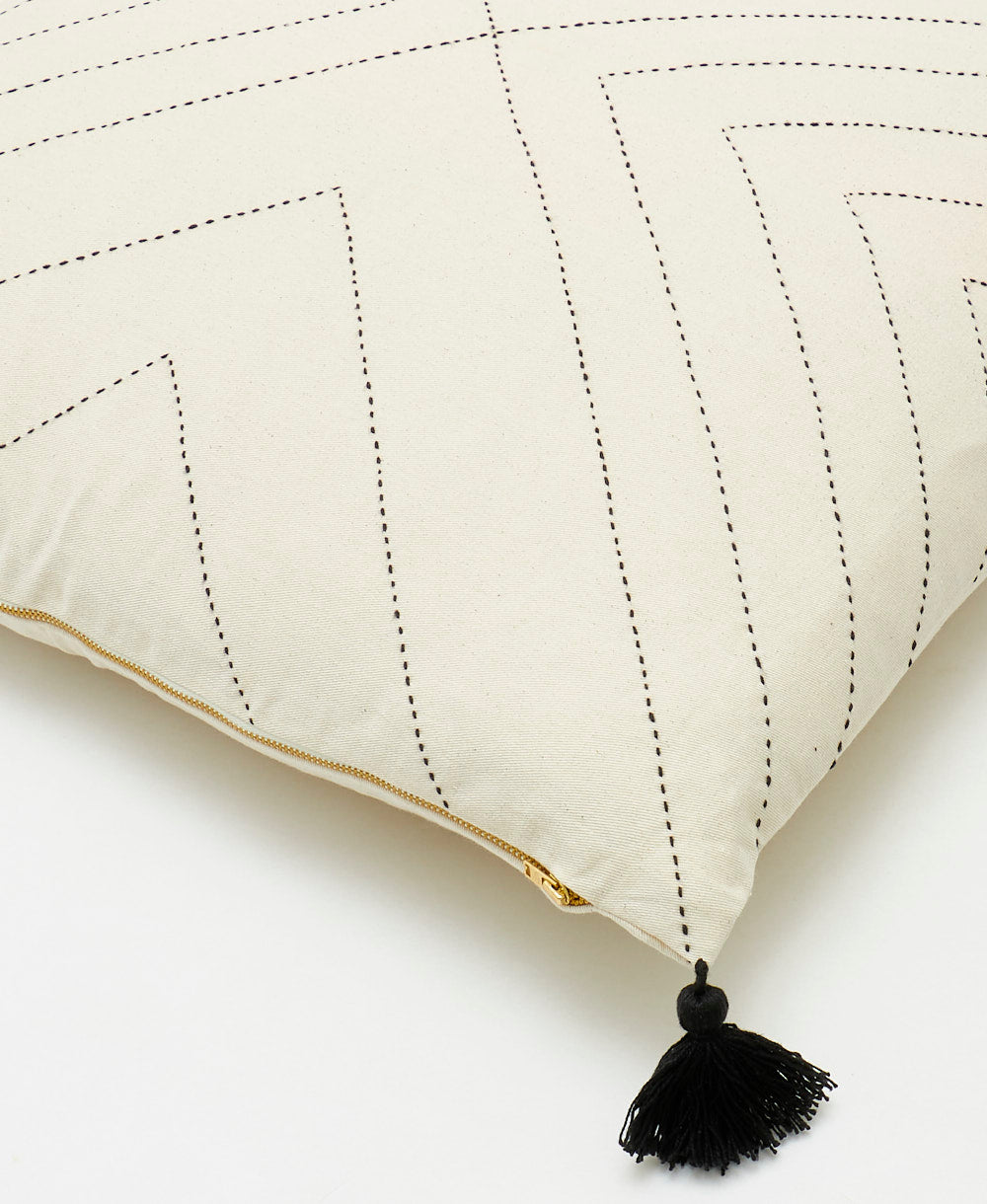 close up detail of white throw pillow with black embroidered stitching and black corner tassels