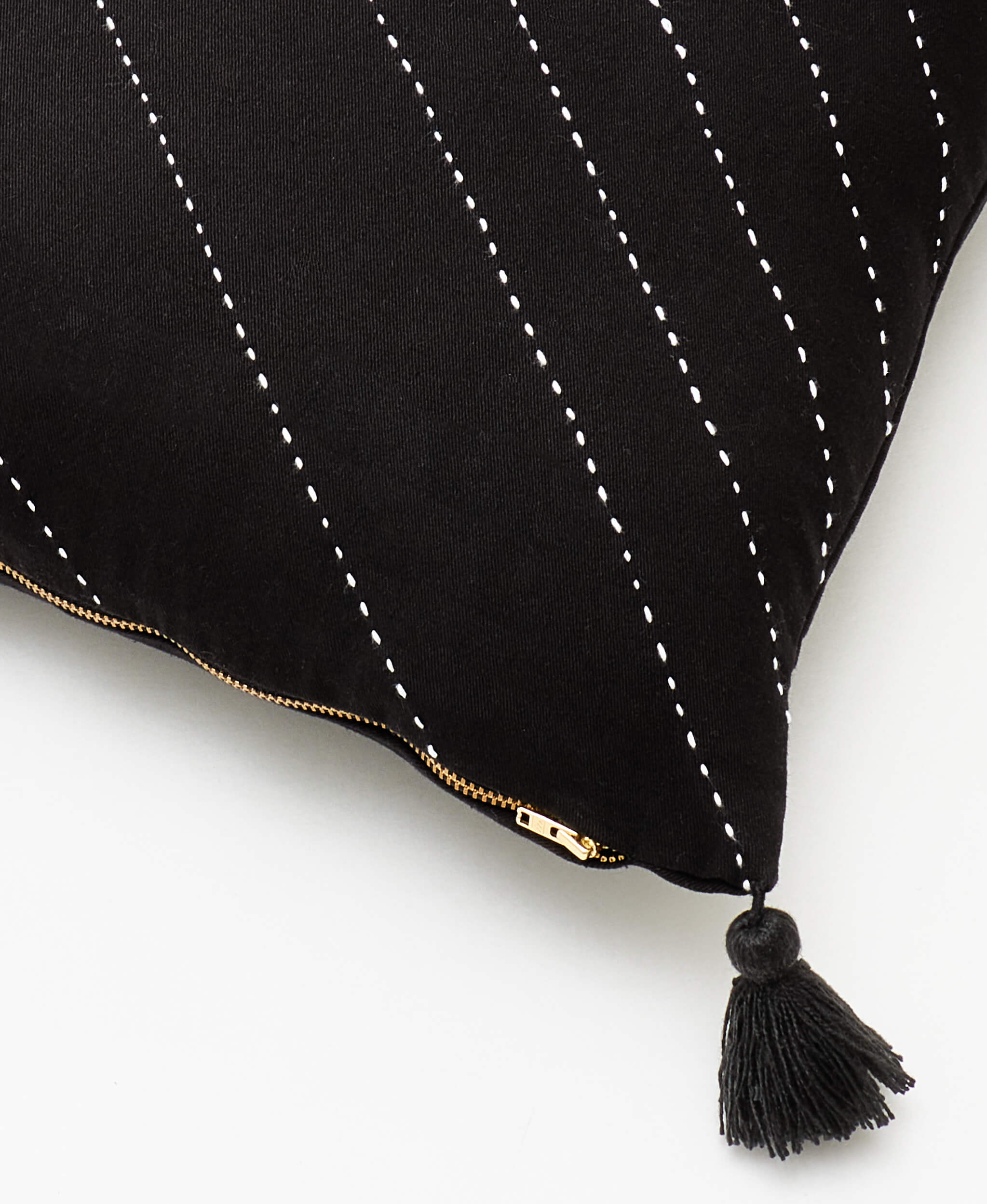 Black pillow with white stitching and a tassel on a white background
