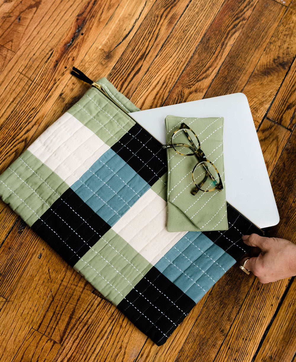 sage green glasses case sitting on matching sage green checkered padded laptop sleeve