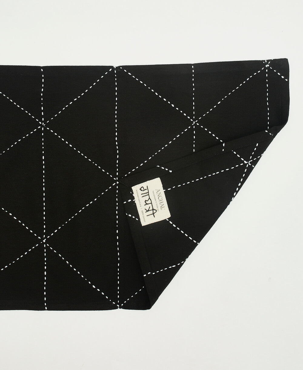 back of a black cotton placemat with white embroidery and the brand tag Anchal with artisan signature