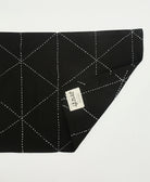back of a black cotton placemat with white embroidery and the brand tag Anchal with artisan signature