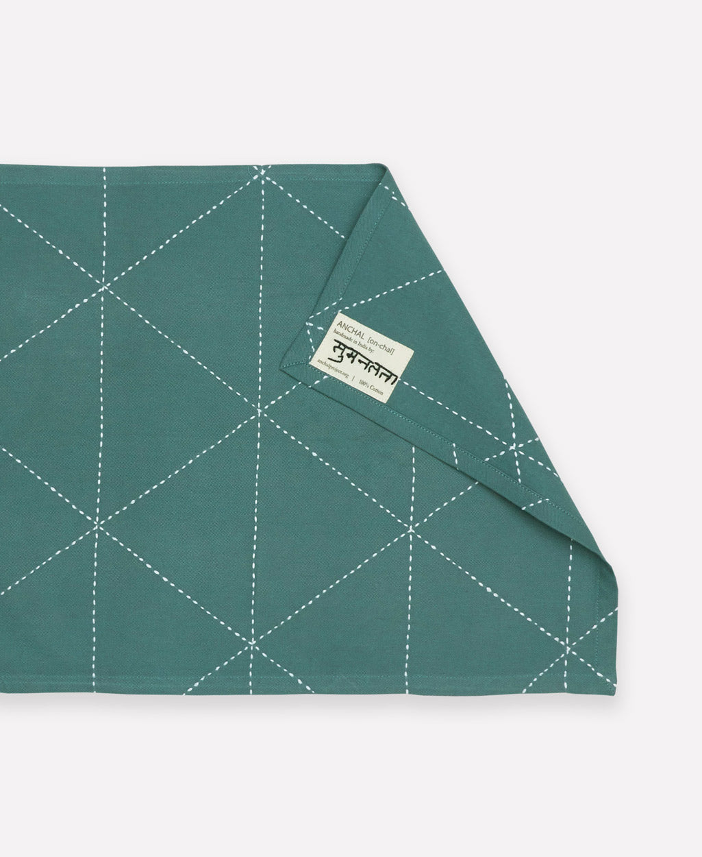 back of spruce green cotton placemat showing brand tag and artisan signature on tag