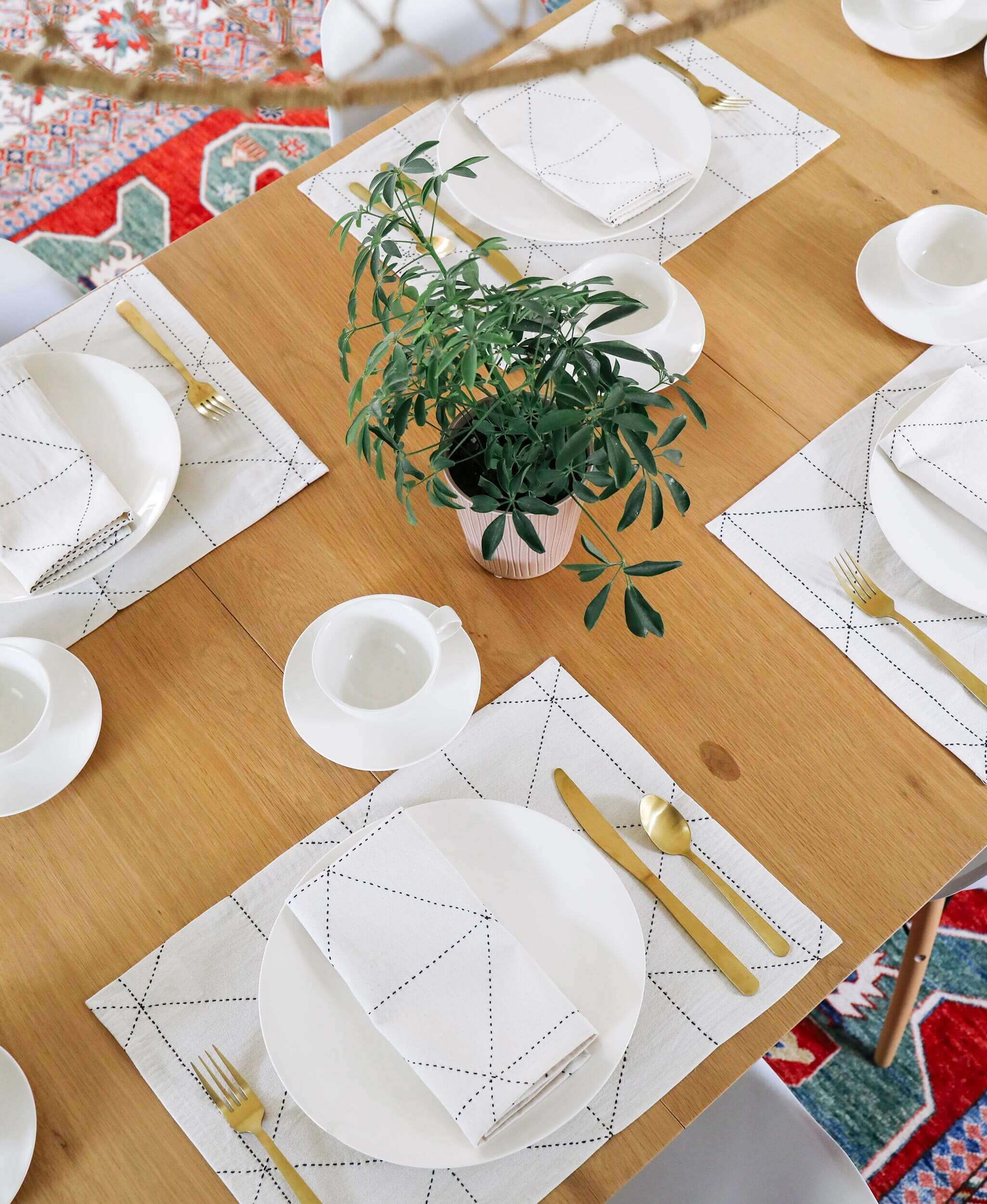 Dining table set with white plates, gold cutlery, and geometric placemats on a wooden table