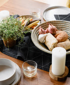 Table setting with bread, vegetables, and a candle on a wooden table with a black embroidered table runner