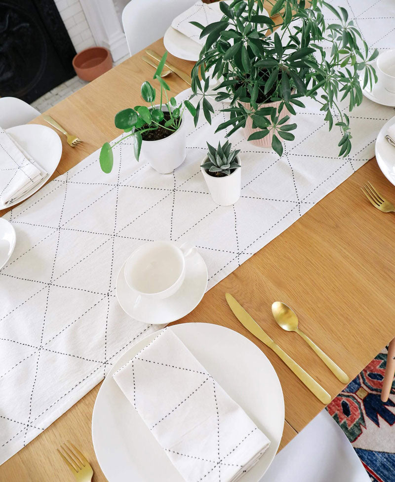 Dining table set with white plates, gold cutlery, and potted plants on a geometric placemat