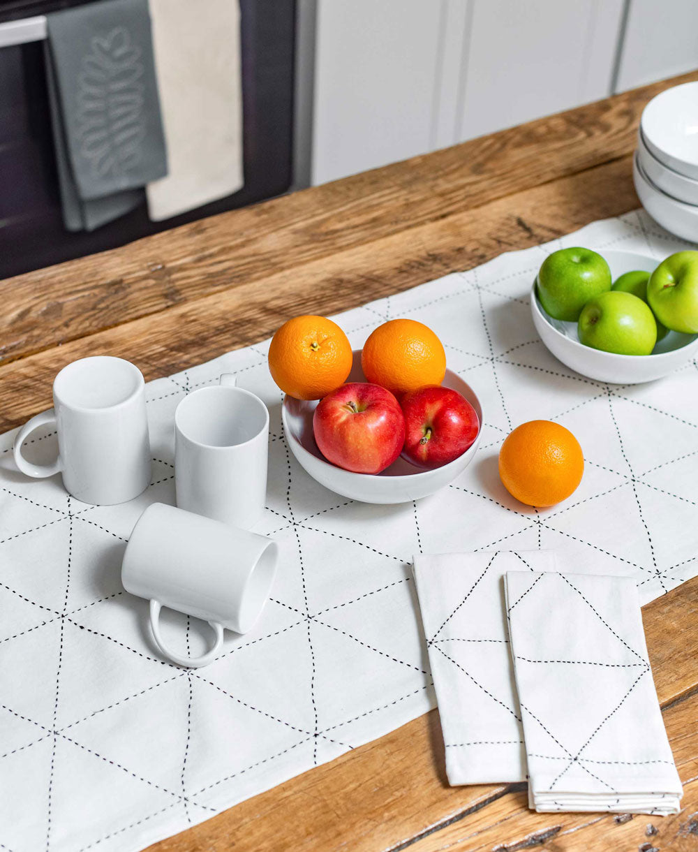 White mugs on a wooden table with fruit bowls and white embroidered napkins