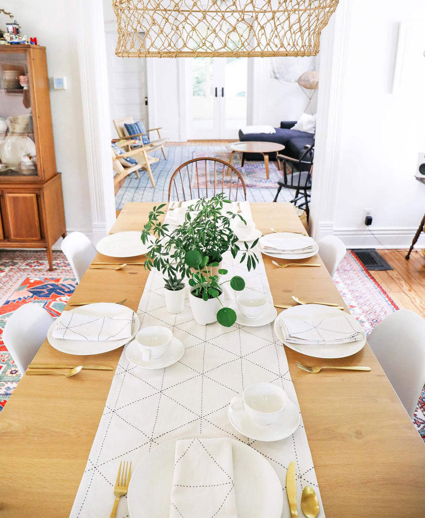 Dining room with a long wooden table set for a meal, featuring white plates, silverware, and a geometric tablecloth