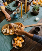 Table setting with bread, pastries, and apricots on a spruce green embroidered tablecloth
