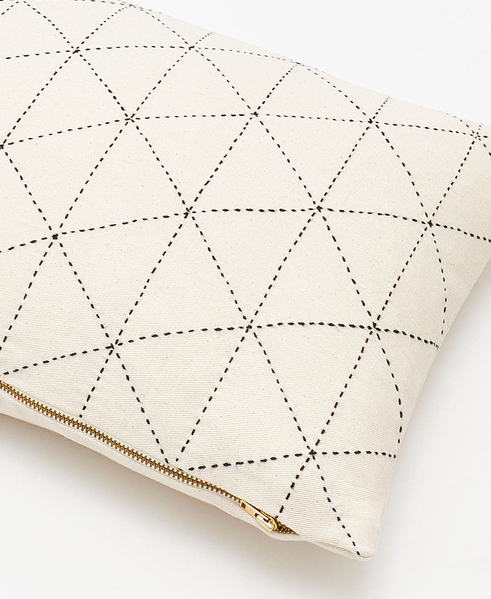 Cream-colored pillow with black geometric stitching and a gold zipper on a white background