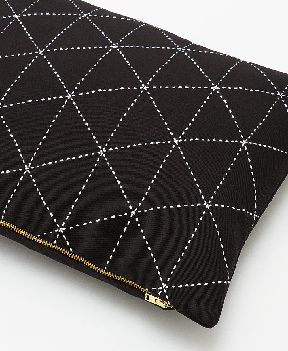 Black pillow with white geometric stitching and a gold zipper on a white background