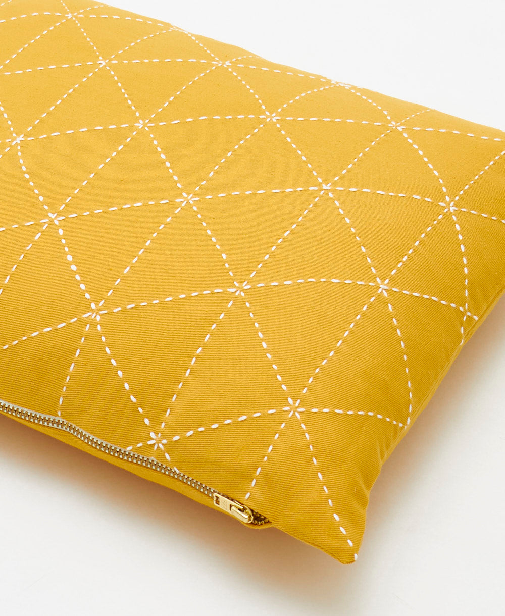 Yellow pillow with white geometric stitching on a white background