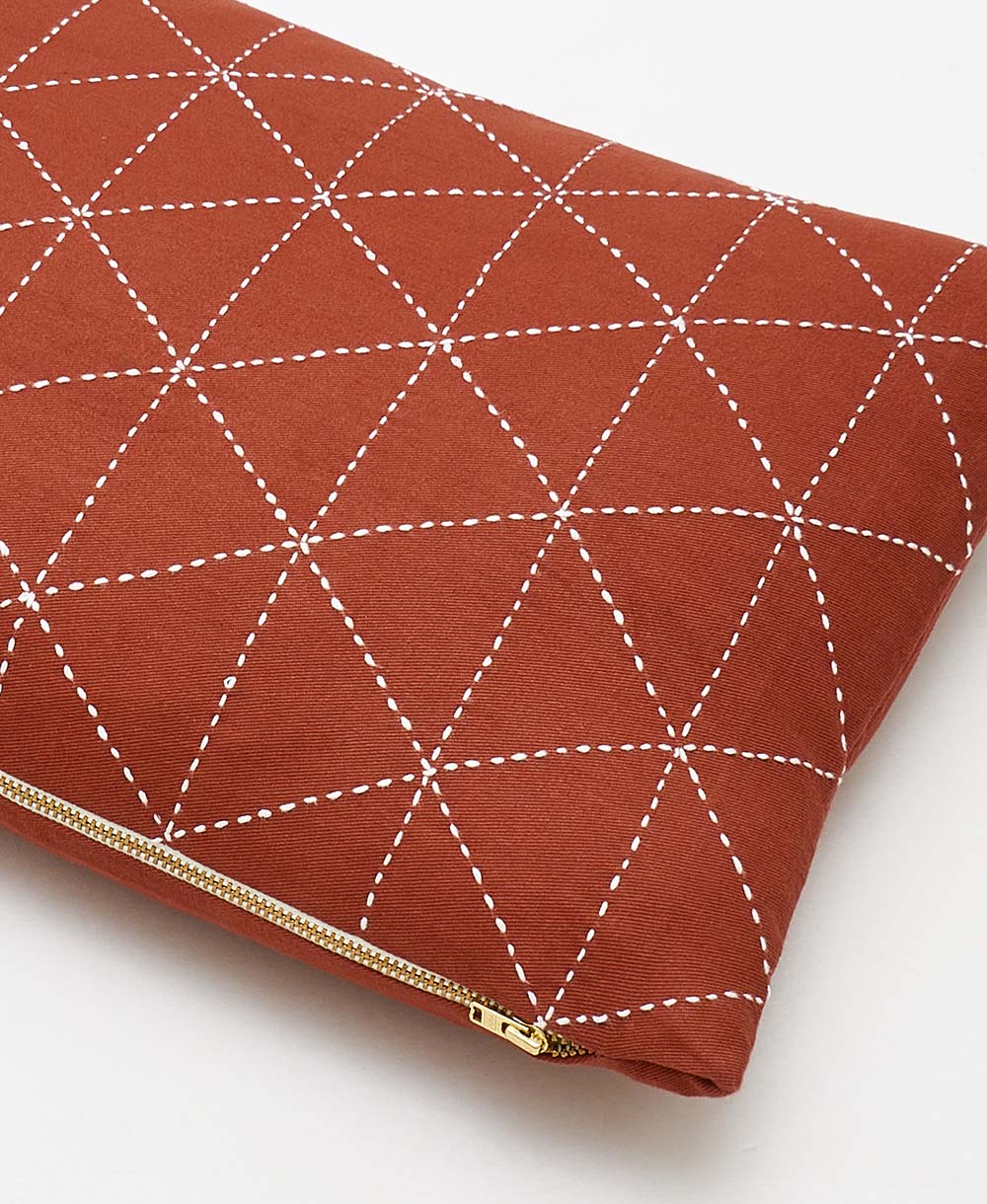 Red clutch bag with white geometric stitching on a white background