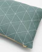 Green pillow with white geometric pattern and gold zipper on a light gray background