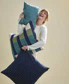 Woman holding three decorative modern pillows against a beige background
